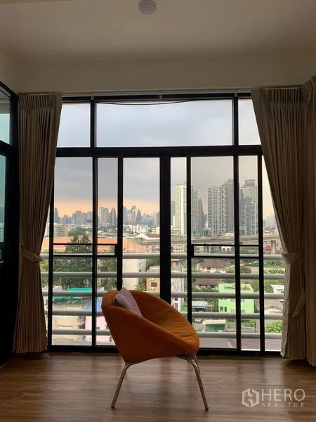 公寓 出租 - 落地窗与城市景观，摆放一把橙色休闲椅。