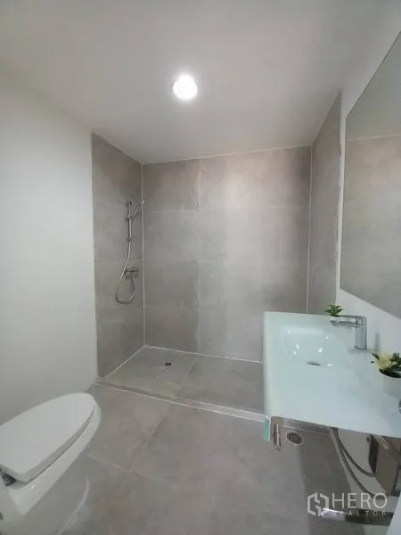 Condominium for rent in Khlong Toei, Bangkok - Modern bathroom with a walk-in shower, large mirror and white fixtures.