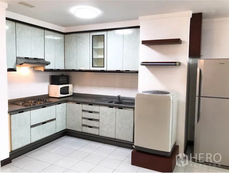 Condominium for rent or sale in Watthana, Bangkok - U-shaped kitchen with upper and lower cabinets, cooktop, range hood, microwave, fridge and washing machine.