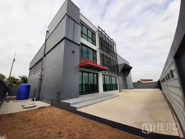 Factory for rent or sale in Lam Luk Ka, Pathum Thani - Side angle of the property with wide concrete driveway, gated entrance and loading bay.
