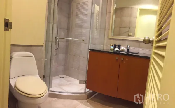 Condominium for rent in Watthana, Bangkok - Modern bathroom with glass-enclosed shower, vanity with black countertop and toilet.