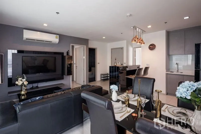 Condominium for rent in Khlong Toei, Bangkok - Living-dining space showing leather sofa, set dining table, and sleek grey kitchen cabinetry.
