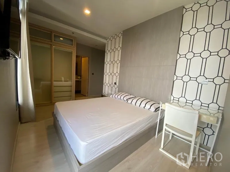 Condominium for rent in Watthana, Bangkok - Primary bedroom with feature wall, bed, desk and mirrored sliding wardrobe.