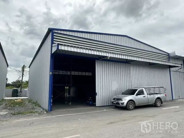 货栈 出租在Khlong Luang, Pathum Thani - 山墙顶仓库外立面，大型卷门开启，皮卡停靠在装卸区。