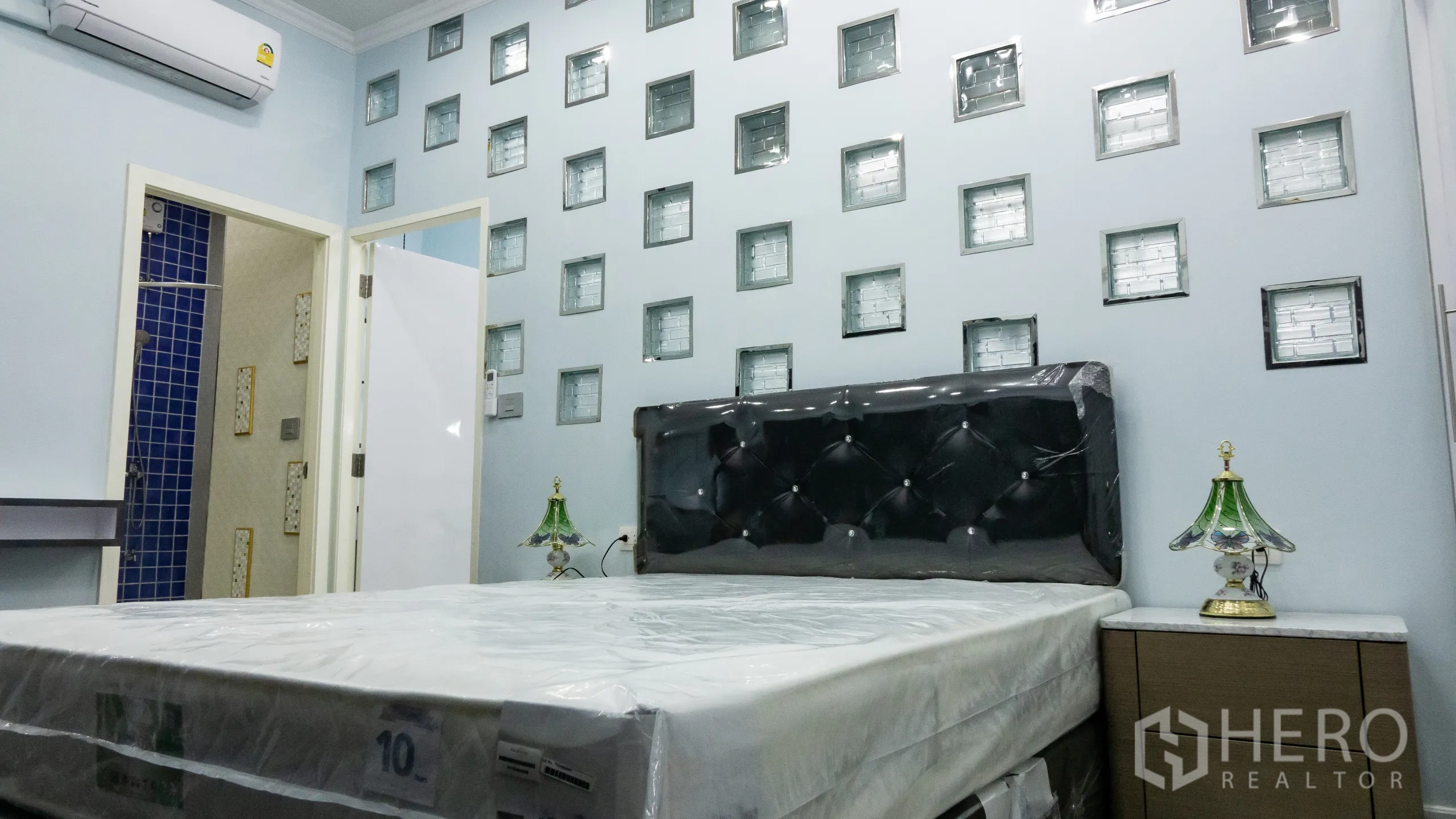 Condominium for rent or sale in Khlong Toei, Bangkok - Master bedroom with tufted headboard, glass‑block accent wall and bedside tables.
