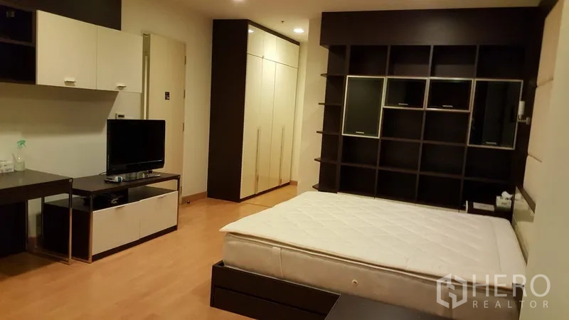 Condominium for rent in Khlong Toei, Bangkok - Spacious bedroom with built-in shelving wall, TV console, wardrobes and wood flooring.