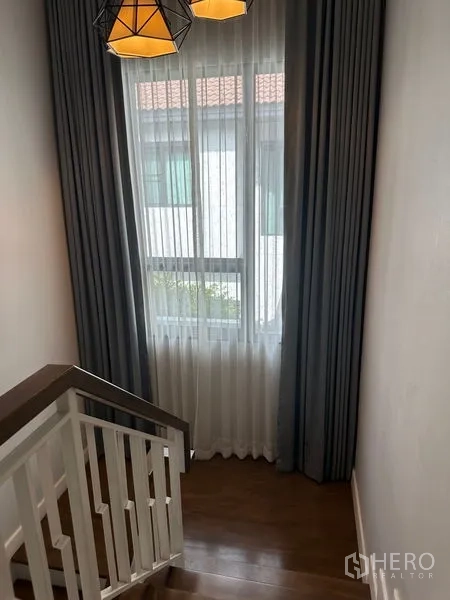 Detached House for rent in Lam Luk Ka, Pathum Thani - Stair landing window with sheer curtains and geometric pendant light.