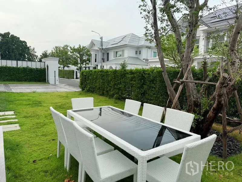 Detached House for rent or sale in Bang Phli, Samut Prakan - Lawn garden with white outdoor dining table and chairs facing a quiet gated community street.
