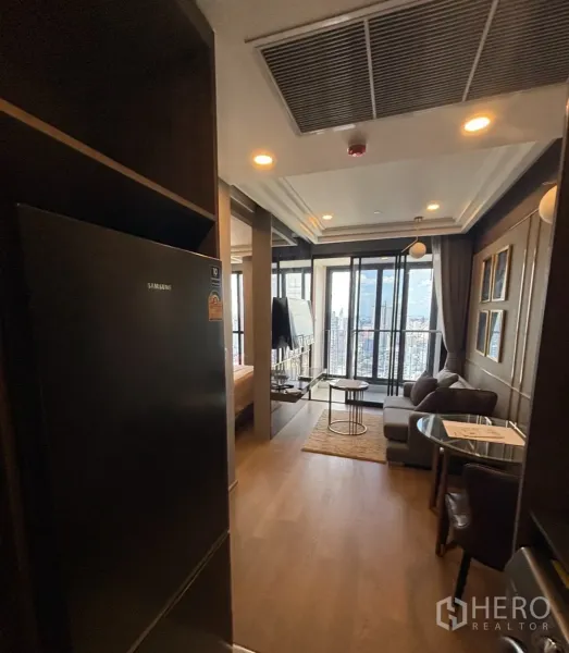 Condominium for rent in Bang Rak, Bangkok - Entry to an open-plan living area with sofa, dining set, TV, tall glass doors to a balcony, and a refrigerator.