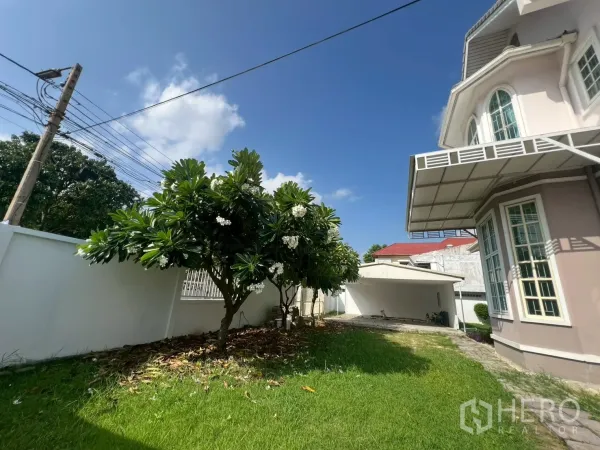 独立式住宅 出售在Phra Khanong, Bangkok - 前院草坪与缅栀子树，靠墙的有顶车棚与房屋一侧。