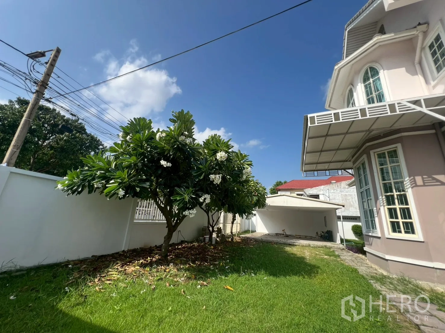独立式住宅 出售在Phra Khanong, Bangkok - 前院草坪与缅栀子树，靠墙的有顶车棚与房屋一侧。