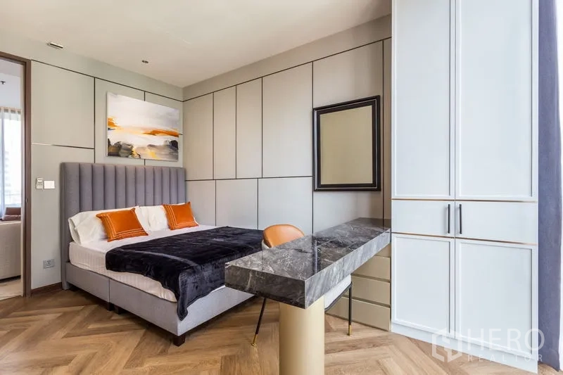 Condominium for rent in Khlong Toei, Bangkok - Stylish bedroom with upholstered headboard, built-in wardrobes and marble-topped vanity.