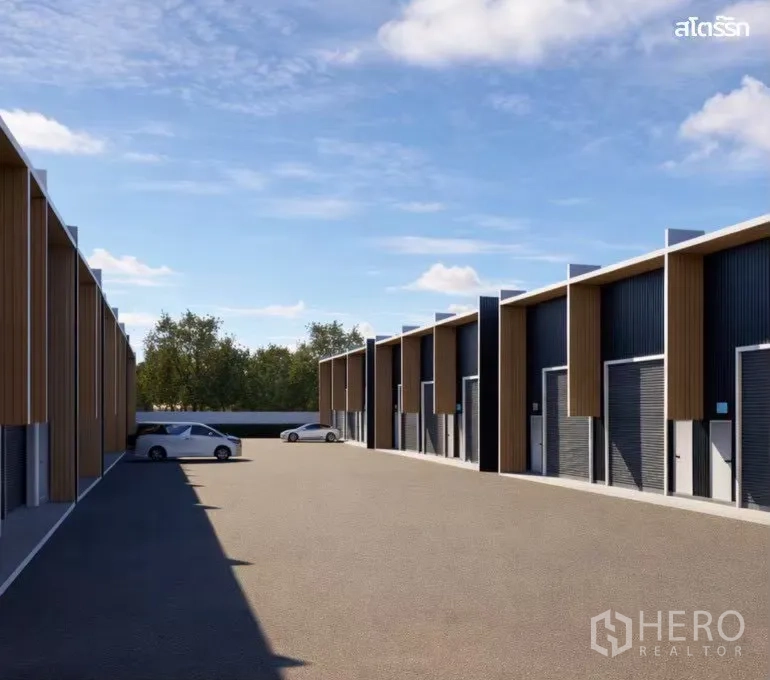 Warehouse for rent in Wang Thonglang, Bangkok - Row of modern warehouse units with roller shutter doors and a spacious paved driveway with parked cars.