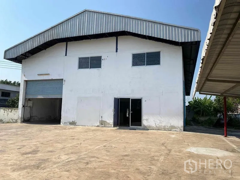 工厂 出租或出售在Bang Phli, Samut Prakan - 工厂正面外观，金属屋顶、卷闸门与玻璃办公入口，前方大型硬化场地。