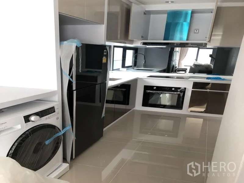 Detached House for rent in Prawet, Bangkok - U-shaped modern kitchen with glossy cabinets, built-in oven, refrigerator and washing machine.