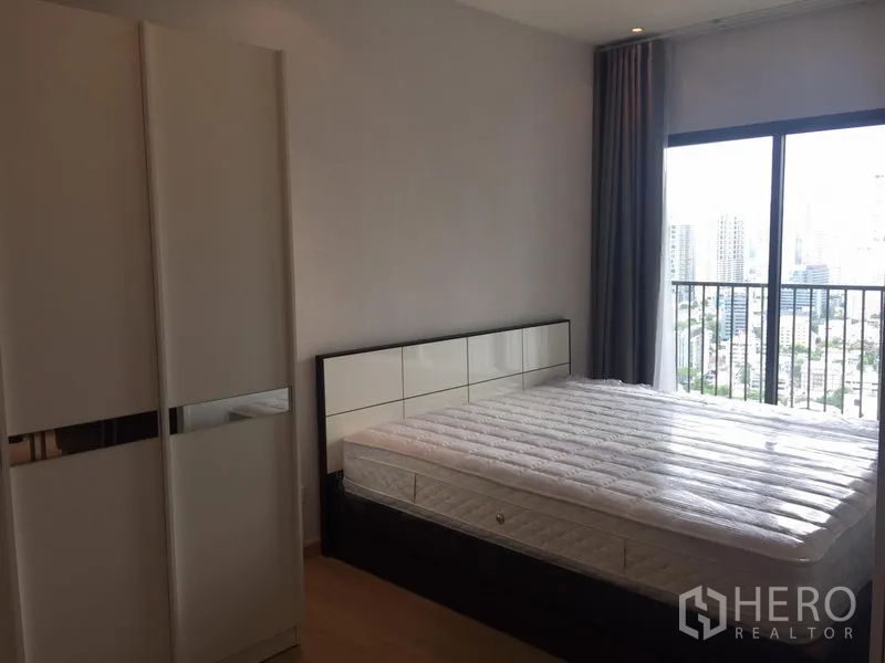 公寓 出租在Khlong Toei, Bangkok - 卧室配大窗与阳台栏杆，可观城市景观，配床与衣柜。