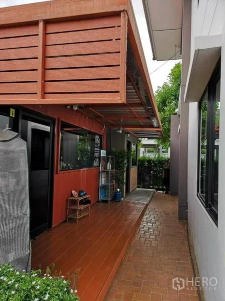 บ้าน ขายในBang Phli, Samut Prakan - ระเบียงด้านข้างมีหลังคาโครงเหล็กสีแดง ทางเดินกระเบื้องและแนวพุ่มไม้ข้างบ้าน