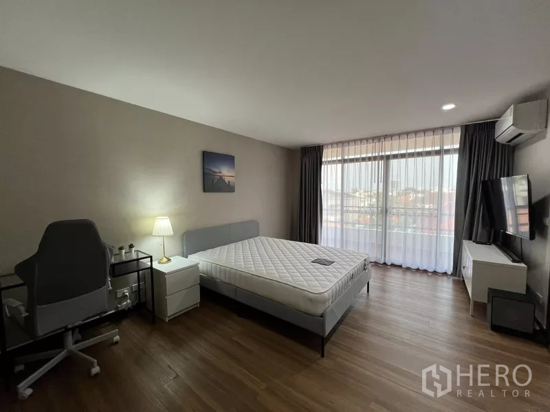 Townhouse for rent or sale in Suan Luang, Bangkok - Sunlit bedroom with bed, work desk, TV and sheer curtains.