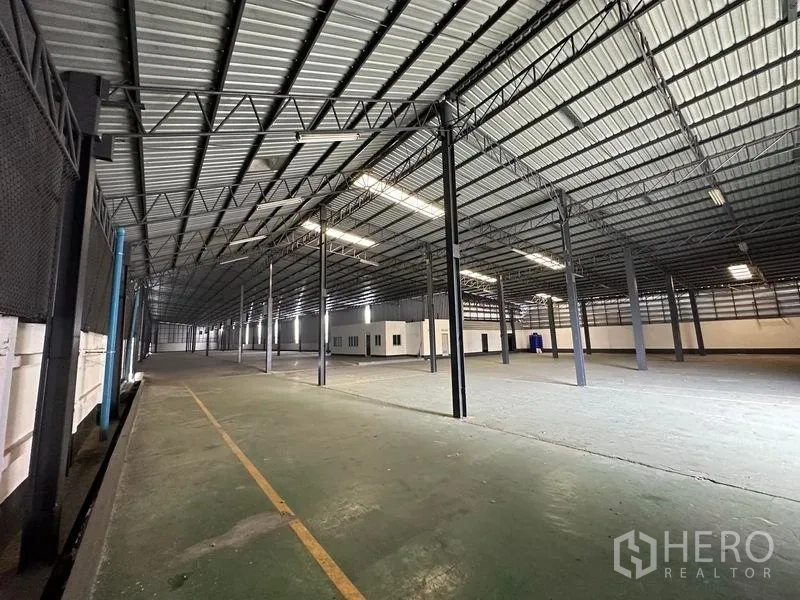 Warehouse for rent in Khan Na Yao, Bangkok - Open storage area under metal truss roof with lane markings and a built‑in office block.