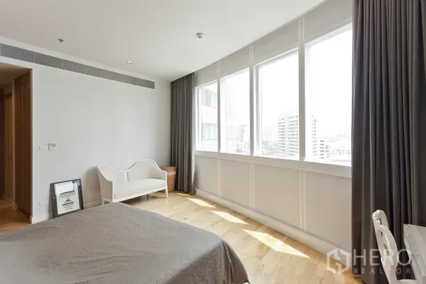 Condominium for rent in Khlong Toei, Bangkok - Sunlit master bedroom with wide city-view windows, hardwood flooring, and curtains.