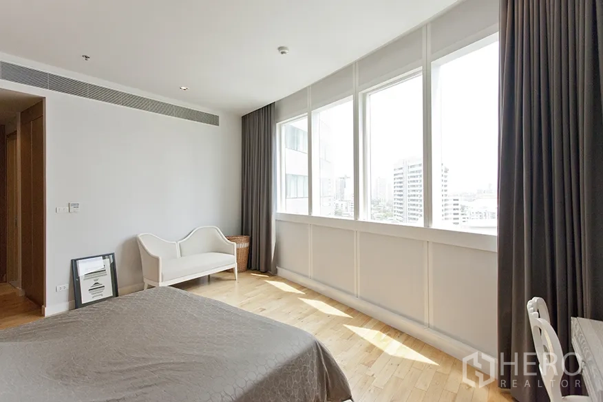 Condominium for rent in Khlong Toei, Bangkok - Sunlit master bedroom with wide city-view windows, hardwood flooring, and curtains.