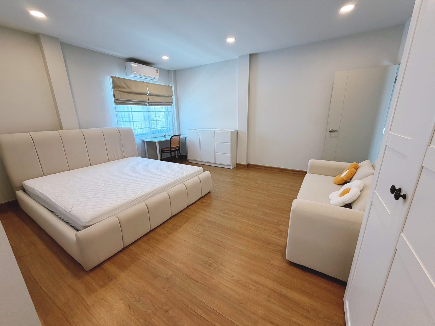 Detached House for rent in Bang Phli, Samut Prakan - Spacious master bedroom featuring upholstered bed, sofa, desk and wood floors.