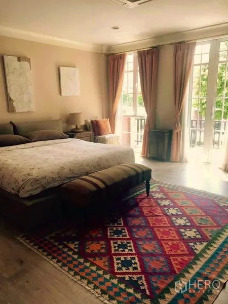 Townhouse for rent or sale in Bangkok - Spacious master bedroom with large windows, balcony doors, patterned rug and soft curtains.