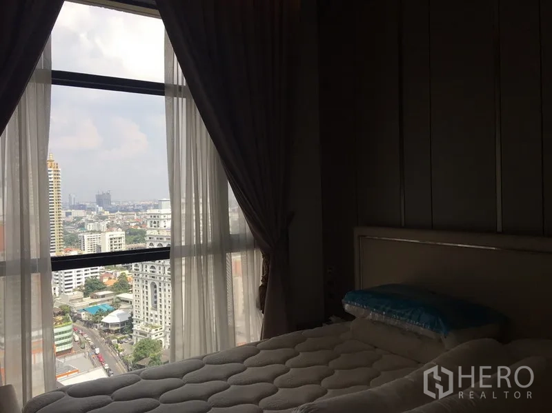 Condominium for rent in Watthana, Bangkok - Bedroom with city skyline view through floor-to-ceiling window and soft drapes.