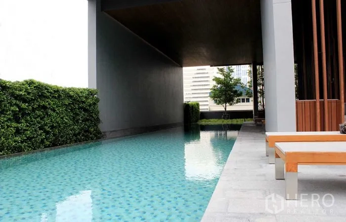 公寓 出租在Watthana, Bangkok - 半室内长泳池，躺椅与绿植的都市公寓配套