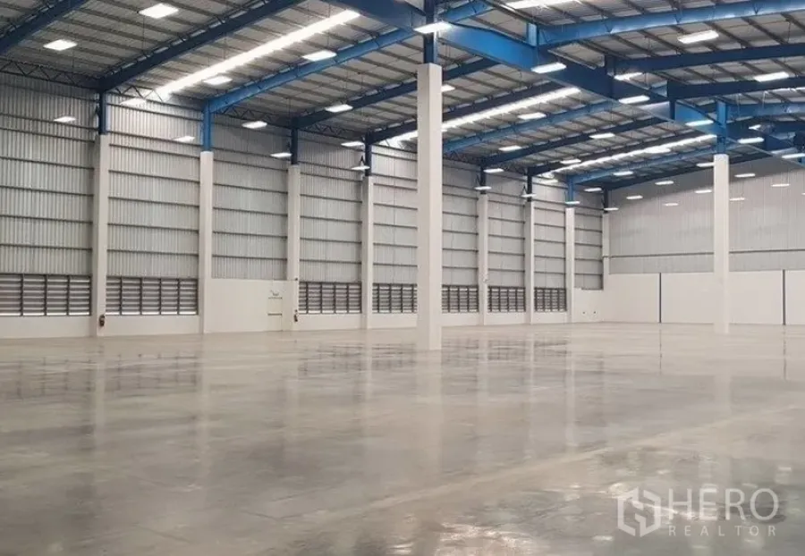 Warehouse for rent in Samut Prakan - Spacious warehouse interior with high clear height, blue steel roof trusses, LED lighting, and polished concrete floor.