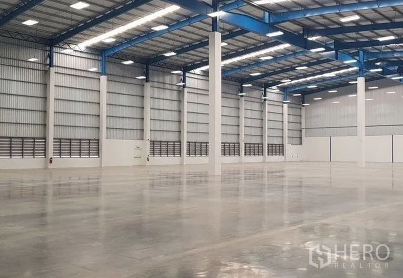 Warehouse for rent in Samut Prakan - Spacious warehouse interior with high clear height, blue steel roof trusses, LED lighting, and polished concrete floor.