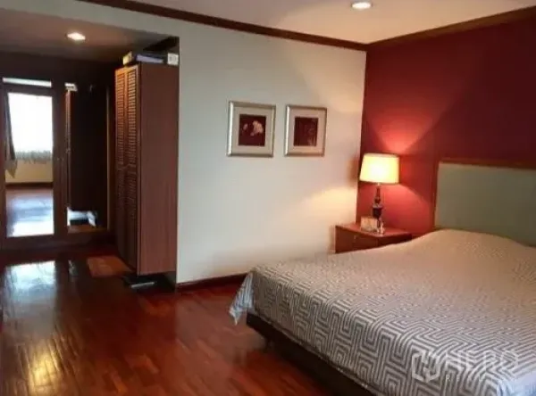 Condominium for rent or sale in Watthana, Bangkok - Master bedroom with hardwood floors, accent wall and bedside lamp.