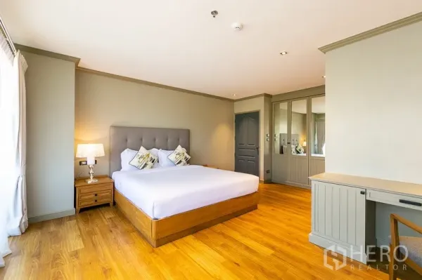 Apartment for rent in Khlong Toei, Bangkok - Spacious bedroom with tufted headboard, bedside lamp, mirrored wardrobe and work desk.