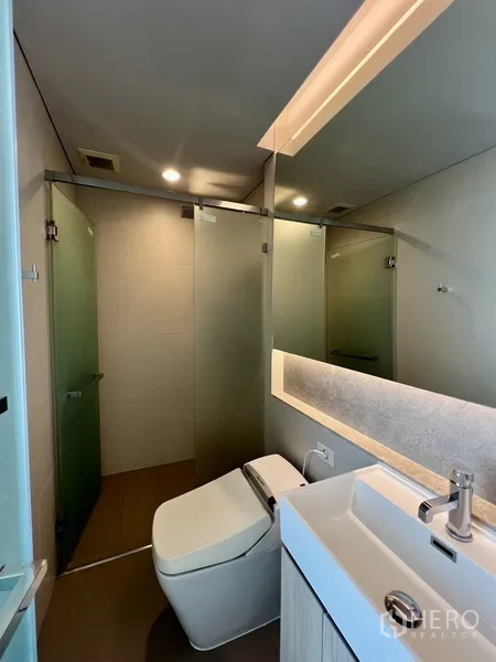 公寓 出租在Khlong Toei, Bangkok - 现代卫浴，玻璃淋浴间、发光镜与简洁洗手台。