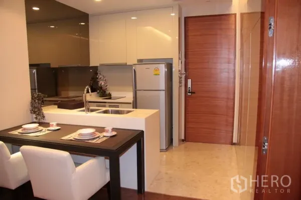 Condominium for rent in Khlong Toei, Bangkok - Modern Bangkok condo entry with sleek kitchen, glossy cabinets, island with double sink, and stainless refrigerator.