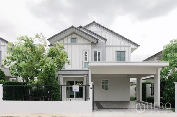 Detached House for rent or sale in Bang Phli, Samut Prakan - Front view of a modern white two-storey detached house with a gated fence and covered carport.