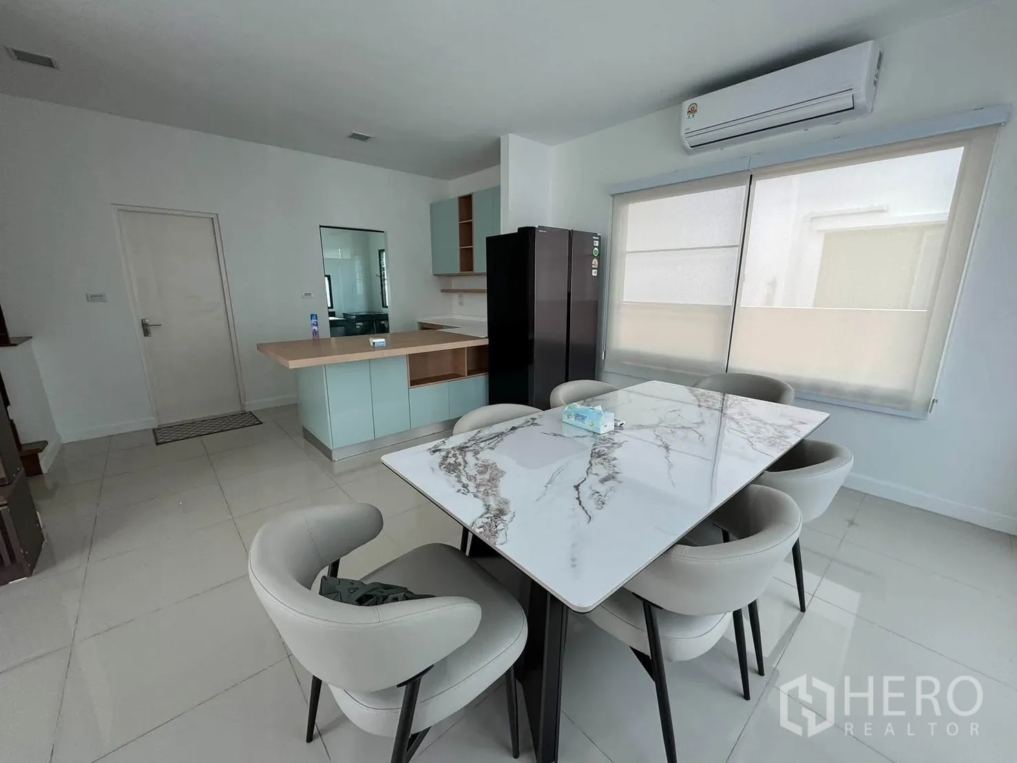 Detached House for rent in Prawet, Bangkok - Dining area with a marble-top table for six beside large windows and an air conditioner.