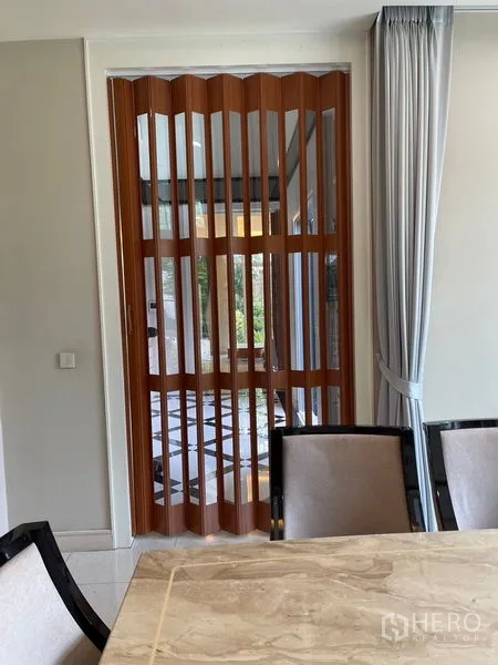 Detached House for rent in Bang Phli, Samut Prakan - Folding wooden slat divider beside the dining area with a marble table and curtains.