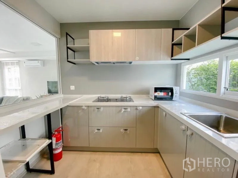 Detached House for rent in Prawet, Bangkok - Modern U-shaped kitchen with gas hob, ample cabinetry and garden-view window.
