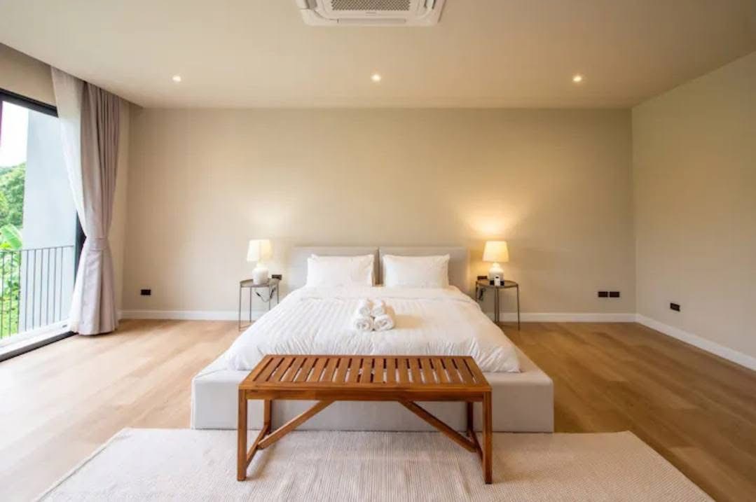 บ้าน ให้เช่าหรือขายในWatthana, Bangkok - ห้องนอนกว้าง เตียงคิงส์ไซส์ ม้านั่งไม้ โคมไฟข้างเตียง แสงไฟดาวน์ไลท์ ใกล้ระเบียงวิวต้นไม้