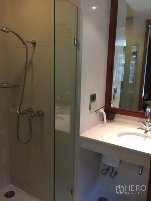 Condominium for rent in Pathum Wan, Bangkok - Contemporary bathroom with glass-enclosed shower and sleek vanity with mirror.