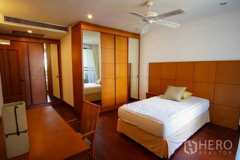 Apartment for rent in Watthana, Bangkok - Bright bedroom with wood paneling, ceiling fan, built-in wardrobe, and study desk.