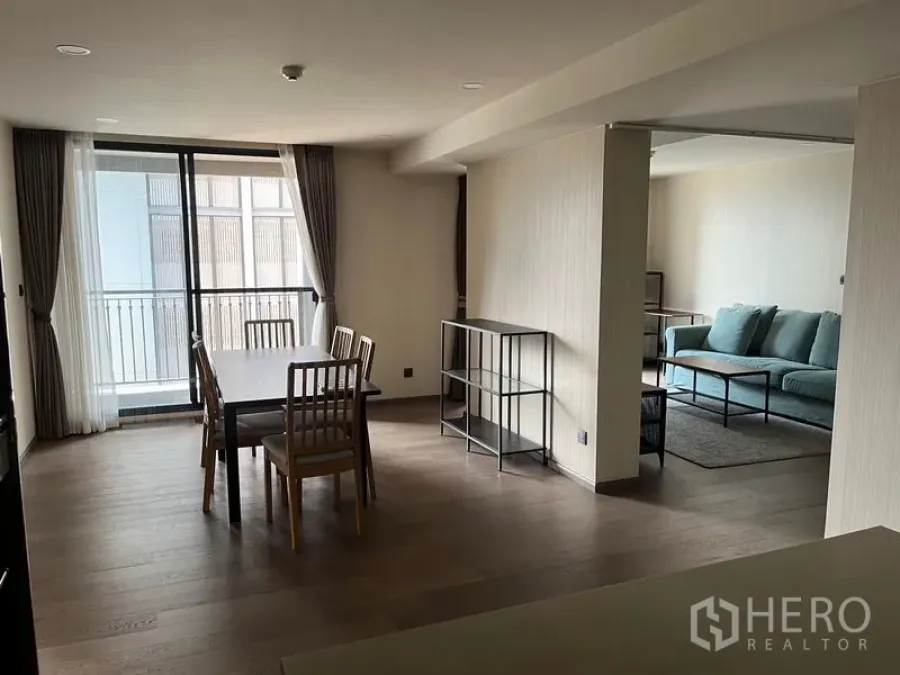 公寓 出租在Pathum Wan, Bangkok - 餐区通向阳台，旁接客厅，配绿色沙发，极简风格室内。