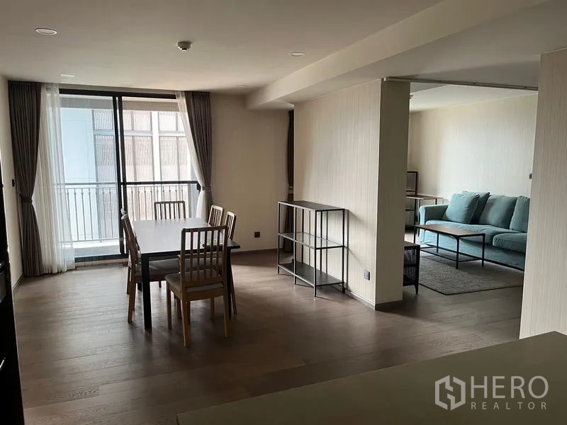 公寓 出租在Pathum Wan, Bangkok - 餐区通向阳台，旁接客厅，配绿色沙发，极简风格室内。