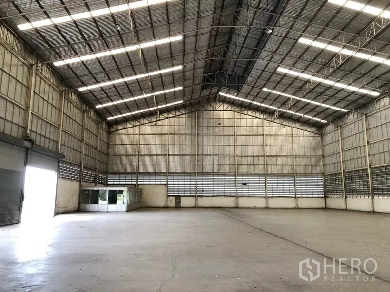 Warehouse for rent in Phra Nakhon Si Ayutthaya - Warehouse interior showing a roller shutter entrance and a corner glass office under a high ceiling.