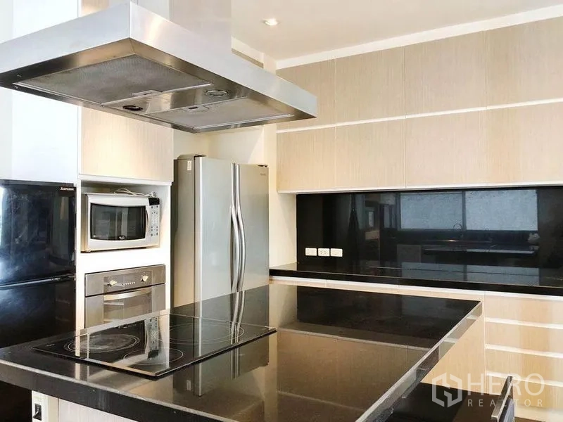 Condominium for rent in Khlong Toei, Bangkok - Modern kitchen with black stone island, induction hob, stainless range hood and double-door refrigerator.