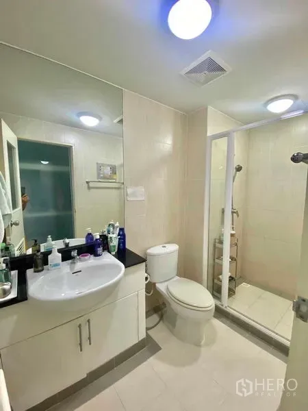 Condominium for rent in Watthana, Bangkok - Modern bathroom with vanity, toilet, and a glass-enclosed walk-in shower under ceiling lights.