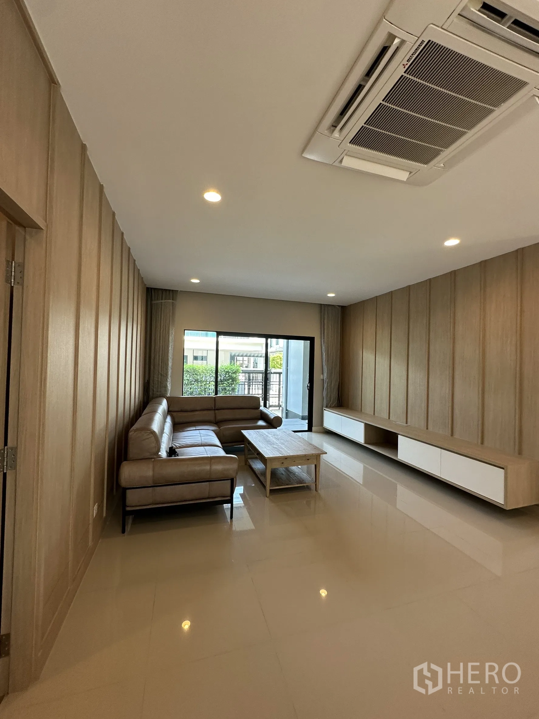 Detached House for sale in Lam Luk Ka, Pathum Thani - Bright living room with L-shaped leather sofa, wood feature wall and cassette air conditioner.