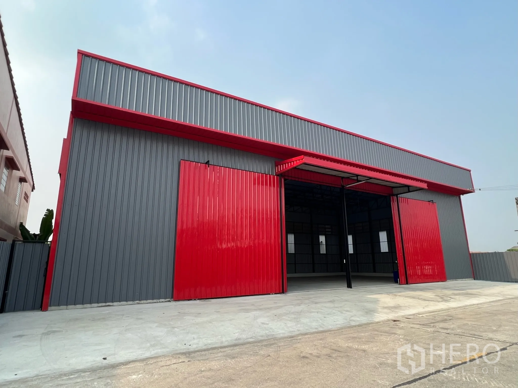 Warehouse for rent in Lam Luk Ka, Pathum Thani - Modern grey-and-red warehouse exterior with wide sliding doors and a concrete loading apron.