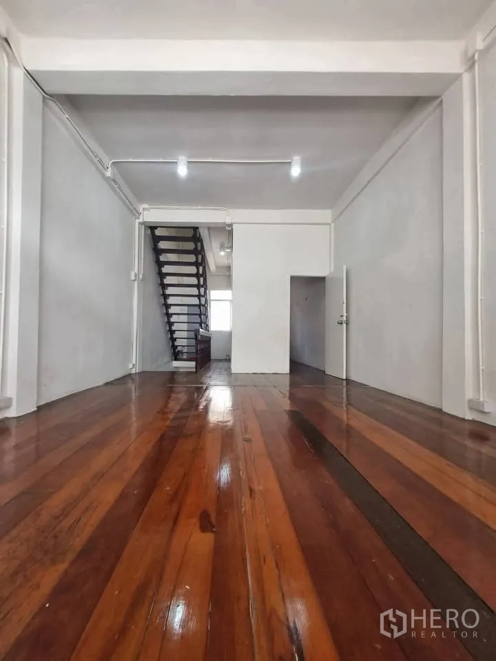 Shophouse for rent in Phra Khanong, Bangkok - Upper-floor room with polished wooden floors, white walls, and a staircase at the back.